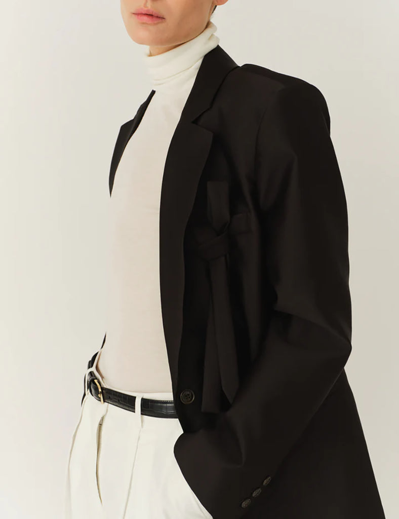 Klasyczna, jednorzędowa marynarka Umami Black o prostym kroju i długości za biodra. Zapinana na dwa guziki. Marynarka ma klapy i trójkątny dekolt. Posiada dwie, przednie kieszenie z klapkami. Wyróżnia się pięknym detalem przypominającym kokardę na kieszeni na piersi.&nbsp;