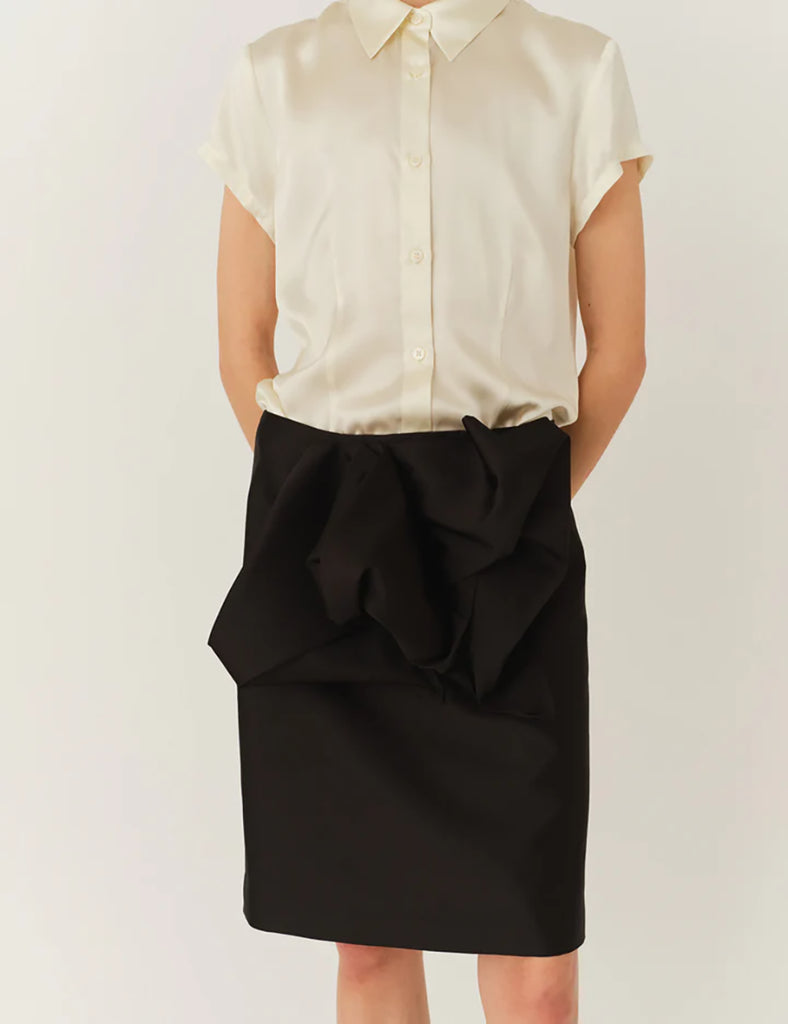 Czarna spódnica Umami Black z wysokim stanem, wykonana z delikatnie połyskującej tkaniny. Wyróżnia się efektownymi detalami z przodu. Zapinana na zamek z tyłu. Połącz ją z marynarką Umami Black, aby stworzyć kompletny, elegancki look.