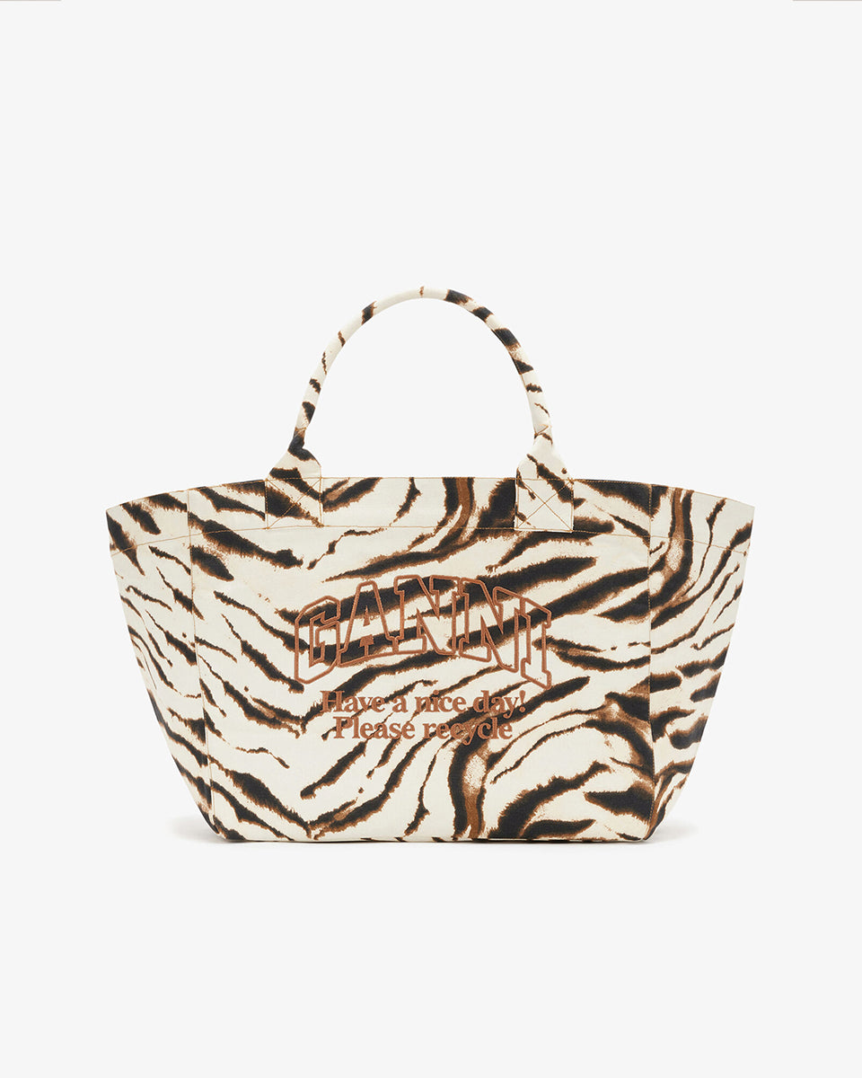 Duża, płócienna torba shopper XXL GANNI w print w zebrę. Z przodu posiada haftowane logo marki i napis "Have a nice day? Please recycle". Torba ma dwie rączki do wygodnego trzymania w dłoni i na ramieniu. Wykonana z grubej, sztywnej, bawełnianej tkaniny. Idealna na zakupy, do pracy, a nawet na siłownię czy weekendowy wypad za miasto.&nbsp;