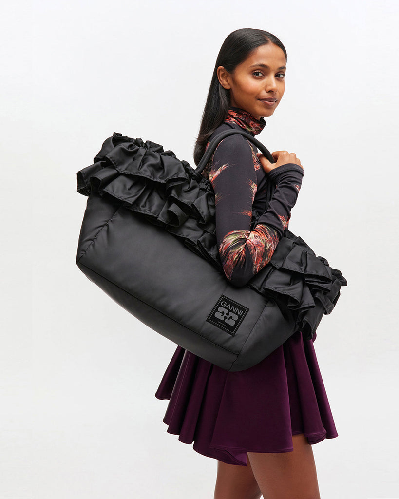 Torba typu tote 7188 XXL Shopper Black marki GANNI z uchwytami. Posiada jedną dużą komorę z wewnętrzną kieszenią zapinaną na zamek. U dołu znajduje się niewielkie logo marki. Wyjątkowości dodaje zdobienie w postaci falbanek. Zaprojektowana, aby pomieścić telefon, portfel, okulary przeciwsłoneczne, klucze, butelkę z wodą, saszetkę, strój sportowy i laptopa.