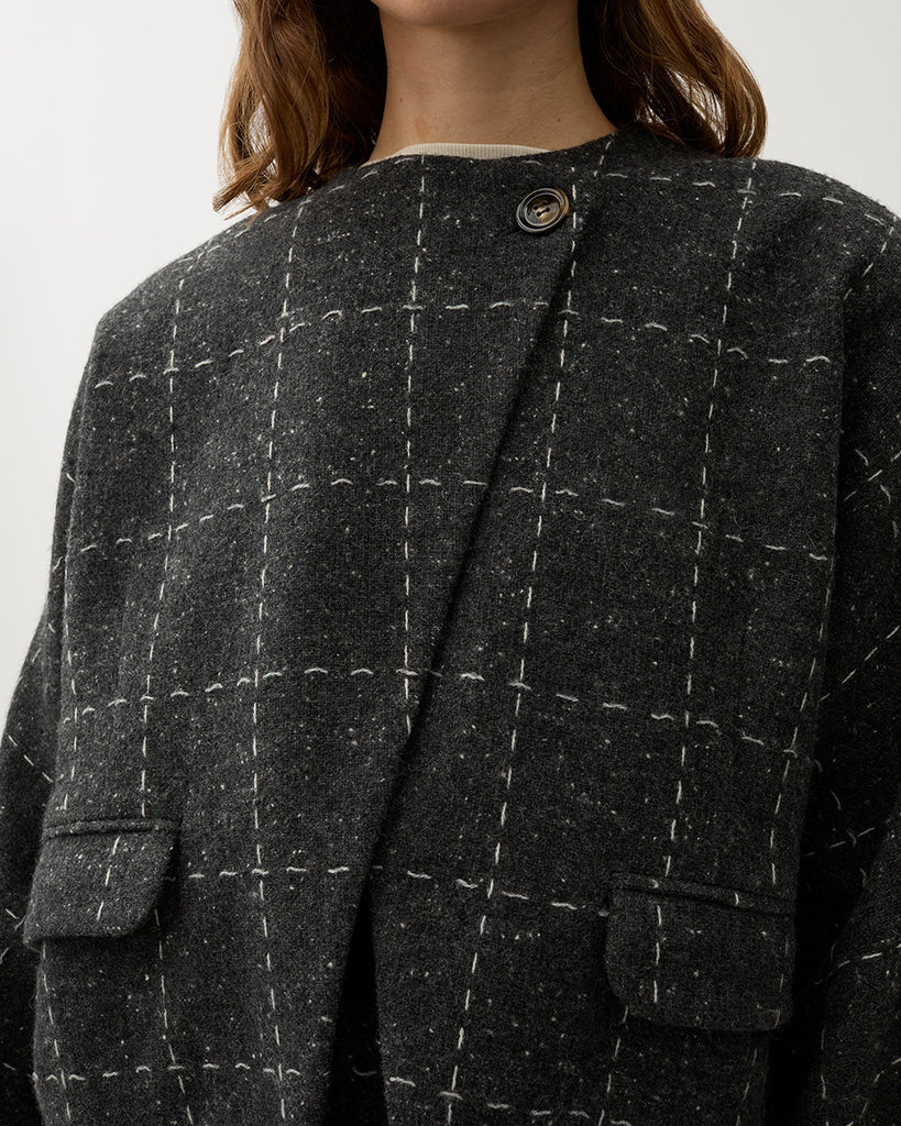 Krótka, luźna marynarka Zola Check Grey Melange w kolorze ciemnoszarym w kratkę z szerokimi rękawami i okrągłym dekoltem. Jest zapinana na jeden guzik pod szyją i posiada kieszenie boczne. Wykonana z mieszanki wełny. Zestaw ją z spódnicą Blanket Check lub ulubionymi jeansami.&nbsp;